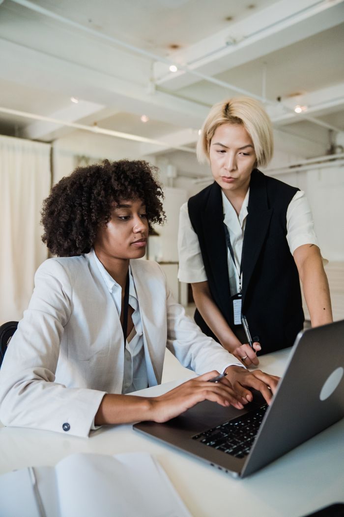Courses A mentor guiding an intern at a laptop in a bright, modern office setting. Professional teamwork emphasized.