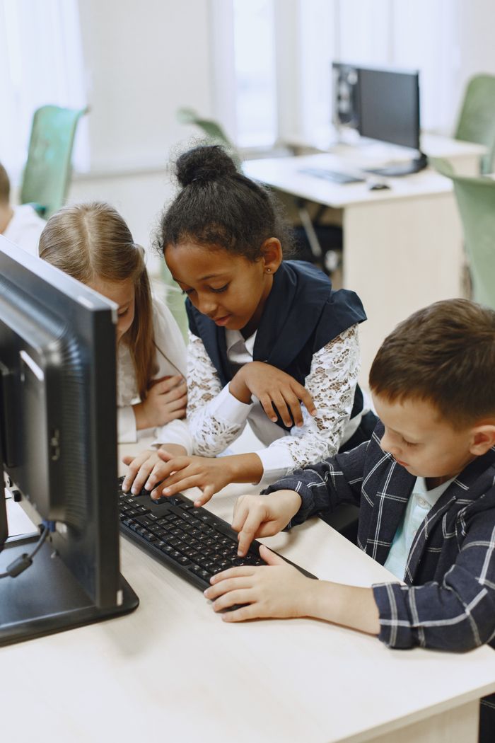 Courses Three children work together on a computer in a school lab, learning and collaborating.