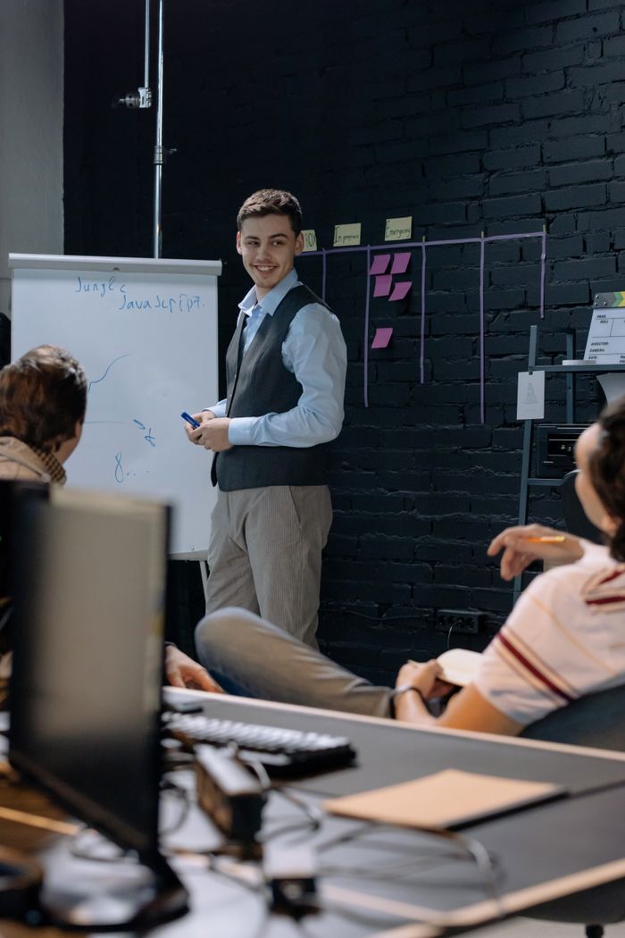 About Young professionals discussing work in an office space while using a whiteboard for presentations and planning.
